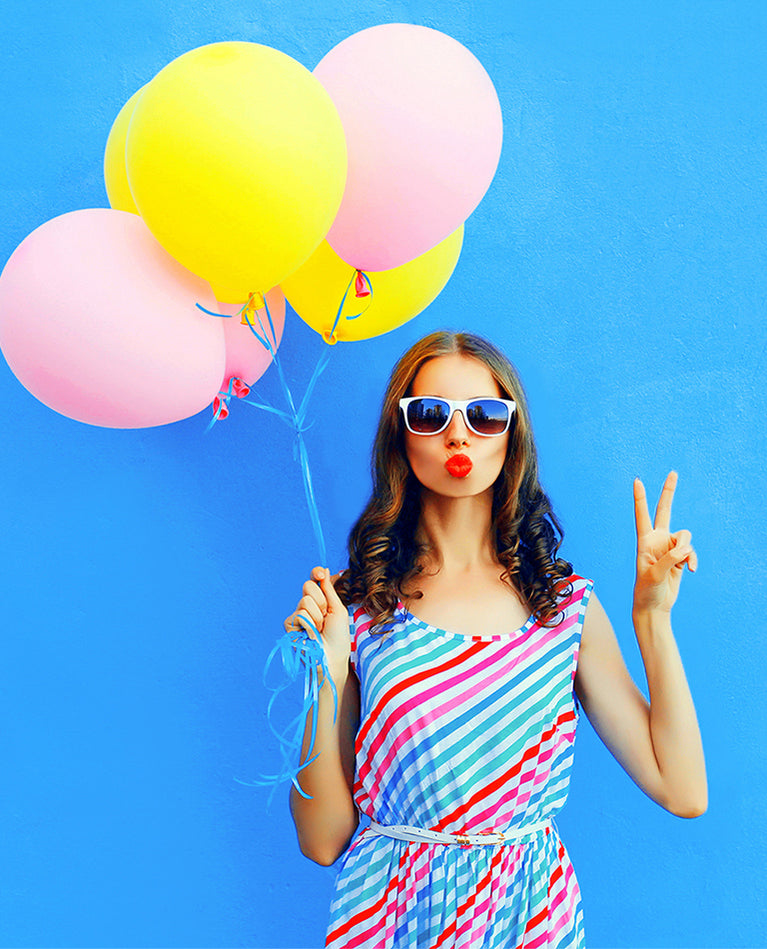 Woman holding colorful balloons against blue wall