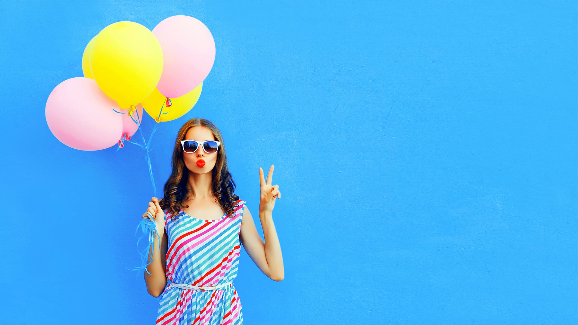 Woman holding colorful balloons against blue wall